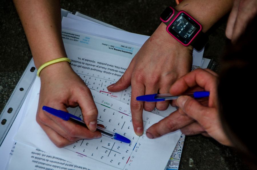 Ruce tří hráčů nad šifrou s mřížkou čísel